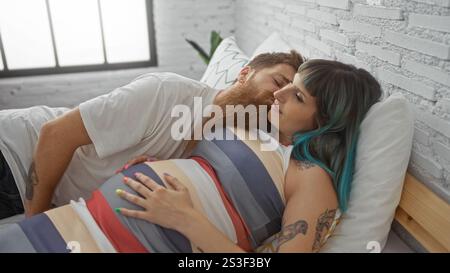 Femme enceinte et homme barbu couchés ensemble sur le lit dans une chambre confortable à la maison, partageant un moment aimant et intime Banque D'Images