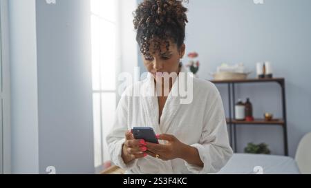 Jeune femme portant une robe blanche à l'aide d'un smartphone dans un salon de spa avec ambiance sereine dans un centre de bien-être Banque D'Images