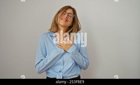 Jeune femme blonde souriant avec les mains sur son cœur, se tenant isolée sur un fond blanc Banque D'Images