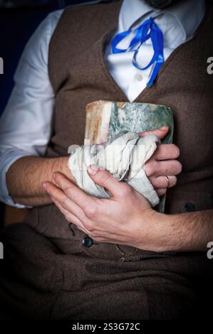 Gros plan des mains d'un homme tenant un vieux livre bien aimé. Sa main gauche est bandée, suggérant une blessure récente. Banque D'Images
