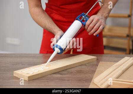 Ouvrier avec pistolet à calfeutrer collant une planche de bois à l'intérieur, gros plan Banque D'Images