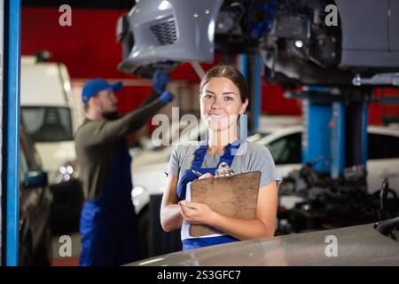 Travailleuse de service automobile tient des registres du travail effectué par les mécaniciens automobiles dans la station-service automobile - prend des notes sur papier Banque D'Images