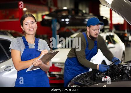 Travailleuse de service automobile tient des registres du travail effectué par les mécaniciens automobiles dans la station-service automobile - prend des notes sur papier Banque D'Images