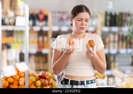 En magasin, la fille frustrée tient les fruits pourris dans les mains. Banque D'Images
