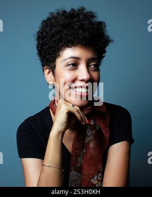 Portrait vertical de belle femme de peau brune souriante et regardant latéralement. Modèle féminin à cheveux bouclés courts. Femme afro-américaine avec le menton sur la main. Banque D'Images