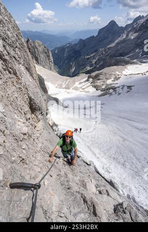 Alpiniste avec casque dans une via ferrata sécurisée, Zugspitz via ferrata, montée à la Zugspitze, derrière le champ de neige du Hoellentalferner et Hoellent Banque D'Images