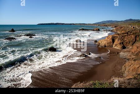 Les vagues roulent sur un rivage accidenté à Cambria, en Californie, en hiver, créant de la mousse blanche lorsqu'elles s'écrasent contre les rochers Banque D'Images