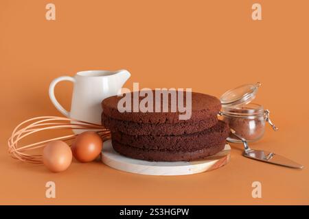 Planche avec des couches de gâteau éponge, des ingrédients et des ustensiles sur fond de couleur Banque D'Images