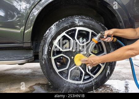 Travailleur lavant voiture suv avec éponge dans le garage. Banque D'Images