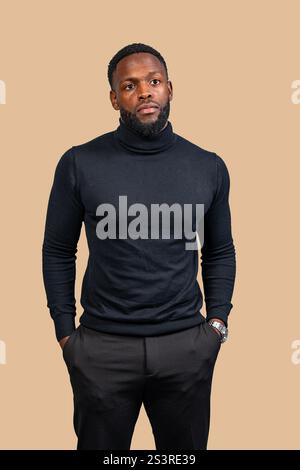 Portrait studio d'un homme d'affaires exsudant la confiance, debout les mains dans les poches, portant un col roulé noir et un pantalon sur fond beige Banque D'Images