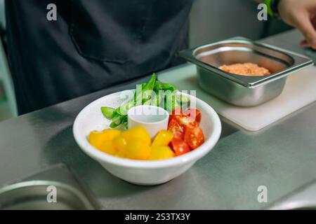 Gros plan sur un chef masculin méconnaissable prépare un bol de poke coloré avec edamame frais, tomates cerises, mangues et saumon. Manger sain COO Banque D'Images