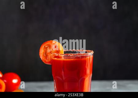 Cocktail secoué de légumes en verre sur fond gris foncé. Cocktail de tomates rouges. Servi avec tranche de tomate. Menu végétalien. Banque D'Images