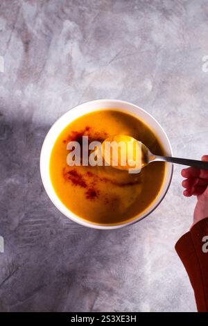 Femme dégustant de la soupe de citrouille avec des épices de paprika et de la crème sur une table blanche. Soupe à la crème plate. Concept de nourriture saine savoureuse. Banque D'Images