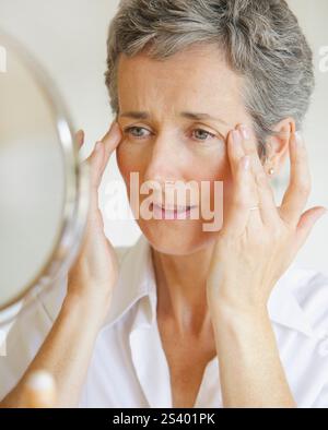 Femme au miroir de toucher ses tempes Banque D'Images