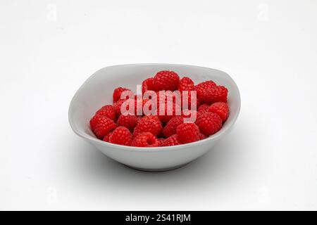Framboises fraîches dans un petit bol blanc sur fond blanc Banque D'Images
