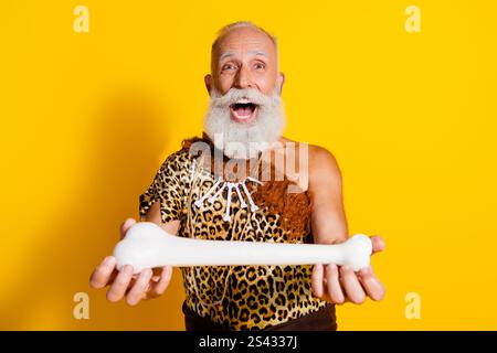 Photo de l'impressionné gars de neanderthal porter la peau léoprad montrant l'espace d'os d'animal emtpy isolé de fond de couleur jaune Banque D'Images