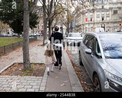 Une femme avec une petite fille marchant dans la rue à Paris avec de beaux bâtiments et des voitures garées. Paris, France - 30 octobre 2024 Banque D'Images