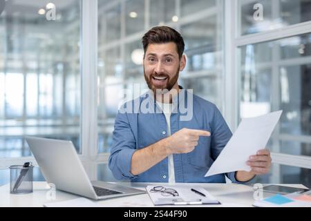 Portrait d'un financier prospère, homme regardant la caméra tenant le rapport financier entre les mains. Homme d'affaires satisfait travaillant avec des documents au lieu de travail à l'intérieur du bureau. Banque D'Images