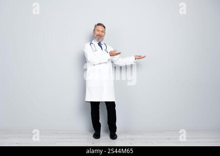Médecin masculin confiant faisant des gestes en uniforme blanc sur un fond gris Banque D'Images