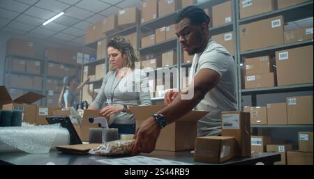 Commis d'entrepôt multiethnique, travailleurs des postes emballage de boîtes en carton avec des commandes en ligne, préparation de colis pour l'expédition aux clients. Centre de tri moderne du magasin de commerce électronique, service de livraison. Banque D'Images