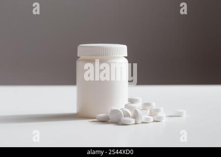 Pilules blanches et bouteille de médecine en plastique sur un fond gris avec espace de copie. Les concepts de médecine et de santé incluent un pot avec des pilules ou des vitamines. Haut- Banque D'Images