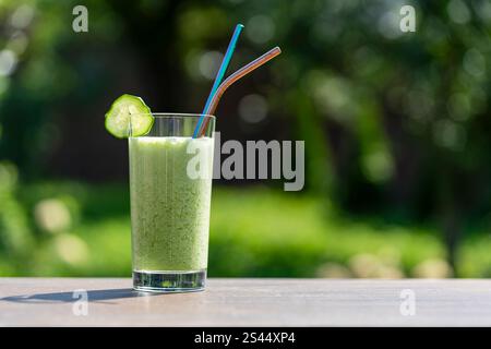 Verre de smoothie vert sur la table en bois dans le café sur fond de nature, gros plan. Boisson biologique saine à base de banane, aneth, persil, concombre A. Banque D'Images