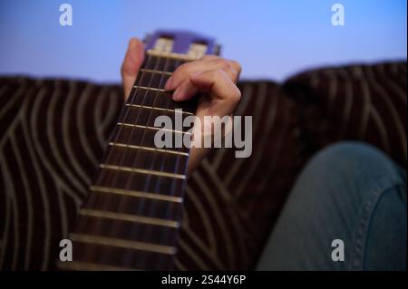 Une main positionnée sur la touche d'une guitare, montrant des cordes complexes. Capturé dans un cadre décontracté avec une ambiance confortable, soulignez Banque D'Images