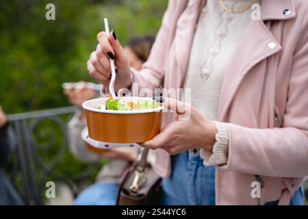 Gros plan des mains d’une femme tenant un bol sans plastique avec une salade fraîche à l’extérieur. L'image met en évidence une alimentation durable, saine et écologique Banque D'Images