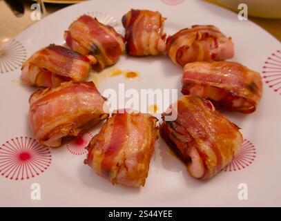 Morceaux de porc avec des crevettes enveloppés dans du bacon sur une assiette blanche à motifs Banque D'Images