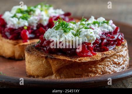 Griller d'une tranche de pain avec du fromage blanc à la crème, de la pulpe de betterave mijotée, des graines et de l'aneth vert sur une planche de bois. Délicieux petit déjeuner le matin. Fermer Banque D'Images