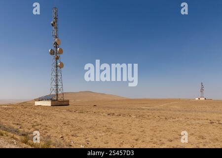Deux tours de communication se dressent dans un paysage sec et aride dans la province de Kunduz, en Afghanistan, sous un ciel bleu clair, mettant en évidence la connectivité à distance. Banque D'Images