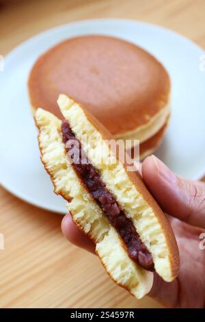 Main tenant un morceau de demi Dorayaki avec Blurry Stack of Whole Cake en toile de fond Banque D'Images