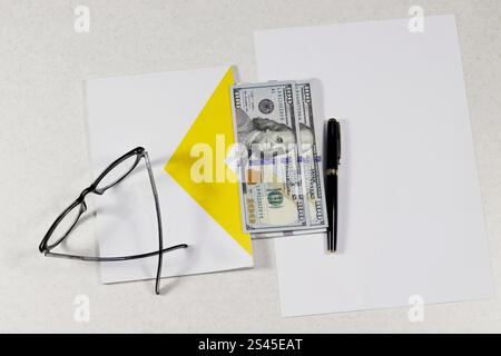 Bloc-notes, lunettes, stylo, feuille de papier vierge, billets de banque américains sur blanc. Banque D'Images
