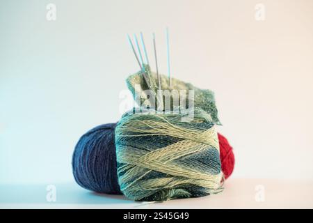 Un projet de tricot mettant en vedette du fil vert étincelant, entouré de fils colorés et d'aiguilles à tricoter, placé sur un fond blanc propre, mettant en valeur Banque D'Images