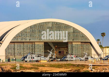 Un hangar avec une grande arche et plusieurs hélicoptères stationnés à l'intérieur. Le hangar est blanc et les hélicoptères sont rouges et blancs Banque D'Images