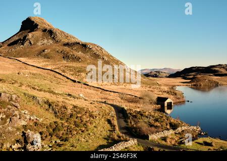 Une maison de bateau se trouve au bord des lacs de Cregennan, ou Llynnau Cregennan, près d'Arthog, Dolgellau, au nord du pays de Galles avec la crête de Pared y Cefn hîr au-dessus. Banque D'Images