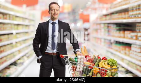 Homme d'affaires dans un supermarché posant avec de la nourriture dans un panier Banque D'Images