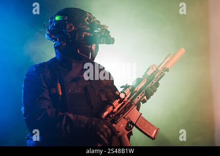 Opérateur tactique équipé d'un équipement militaire avancé et d'un fusil, éclairé avec un éclairage coloré et atmosphérique, créant une représentation puissante et dynamique o Banque D'Images