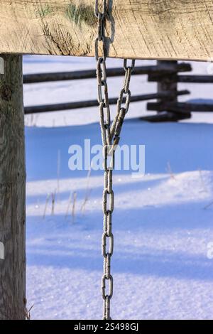 Une chaîne pend à un poteau en bois dans la neige. La chaîne est longue et a une couleur argentée. L'image a une humeur calme et paisible, comme la chaîne est hangin Banque D'Images