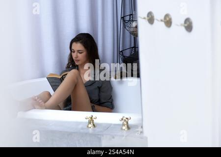 Femme, baignoire et la lecture d'un livre à la maison, la paix et le roman pour la croissance de soi ou l'inspiration. Personne féminine, littérature de confort et fantaisie de fiction Banque D'Images