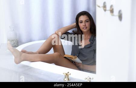 Femme, baignoire et livre de lecture à la maison, portrait et roman pour la croissance de l'autosoin ou l'inspiration. Personne féminine, littérature de confort et fantaisie de fiction Banque D'Images