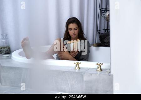 Femme, baignoire et livre de lecture à la maison, passe-temps et roman pour la croissance ou l'inspiration de self-Care. Personne féminine, littérature de confort et fantaisie de fiction pour Banque D'Images