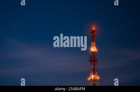 Une imposante structure de communication se dresse contre le ciel nocturne, ses lumières brillent chaleureusement. Étoiles scintillent dans le fond, créant un paisible Banque D'Images