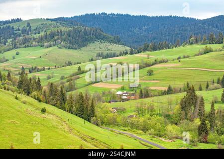 Les collines couvertes de verdure vibrante s'élèvent doucement vers l'horizon, encadrant un village pittoresque. Banque D'Images
