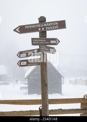Panneau en bois pour diverses attractions touristiques dans la station de sports d'hiver et la ville thermale de Harghita-Băi (hongrois : Hargitafürdő) dans un paysage enneigé. Banque D'Images