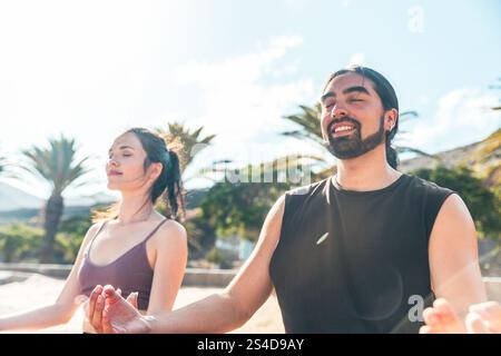 Un homme et une femme sont assis sur la plage, souriant tout en méditant. Banque D'Images