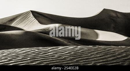 Une photo en noir et blanc d'un paysage désertique avec une grande dune de sable au premier plan. La dune est entourée d'un paysage rocheux et aride. Concept o Banque D'Images