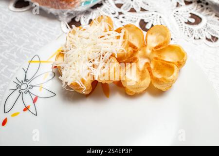 Deux rosettes de gaufres frites en forme de fleurs, remplies de fromage mou râpé Banque D'Images