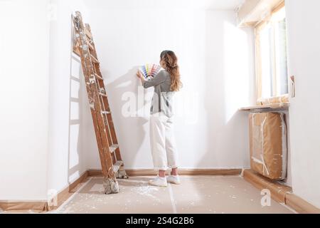 Femme arrière avec des échantillons de peinture choisissant une couleur pour peindre les murs de la maison. Moment de travail de bricolage pour la décoration de la maison, la rénovation et le rafraîchissement appartement dans Banque D'Images