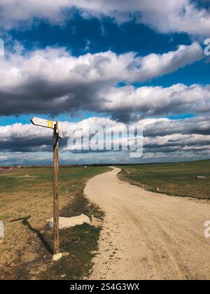 Une route de campagne de gravier serpentant à travers la prairie va au-delà d'un horizon avec des nuages bas dans le ciel printanier. Panneau de signalisation routier. Paysage rural. Banque D'Images